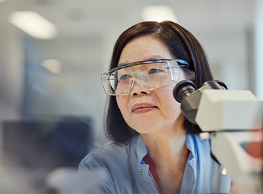 close up of a scientist wearing goggles sitting next to a microscope